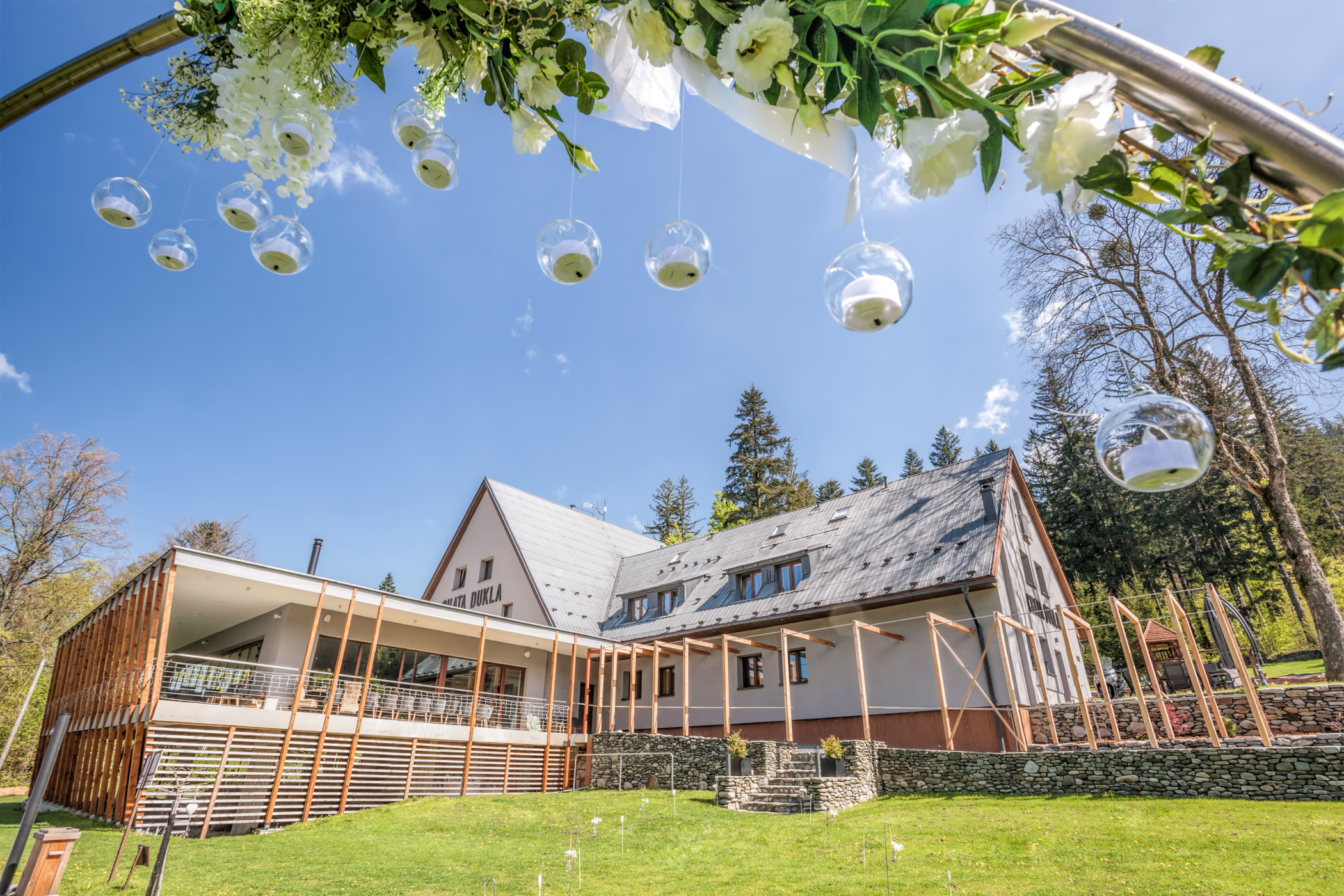 Chata Dukla v Beskydech — venkovní obřadní místo s bílým obloukem z květin a modrou oblohou